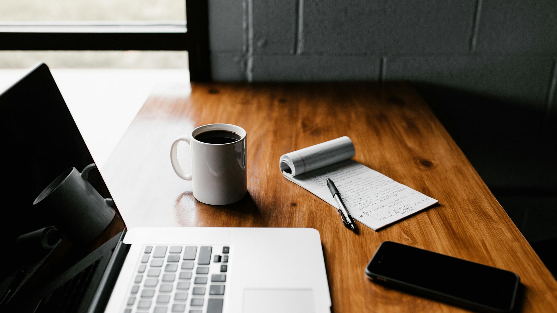 ai safety as a core employee skill -- a macbook, phone, coffee and a notepad on a wooden table